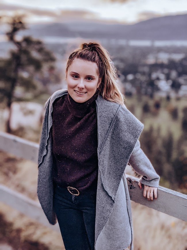 Photo of Kaylin Bennett, wearing a grey swearer with her brown hair up in a pony tail as she poses for the photo, the new Interior Design Assistant at Creative Touch Interiors.